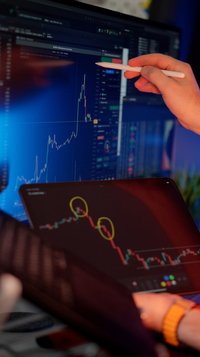 Trader pointing at a candlestick chart on a monitor